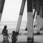 mother and young son stand underneath ocean pier