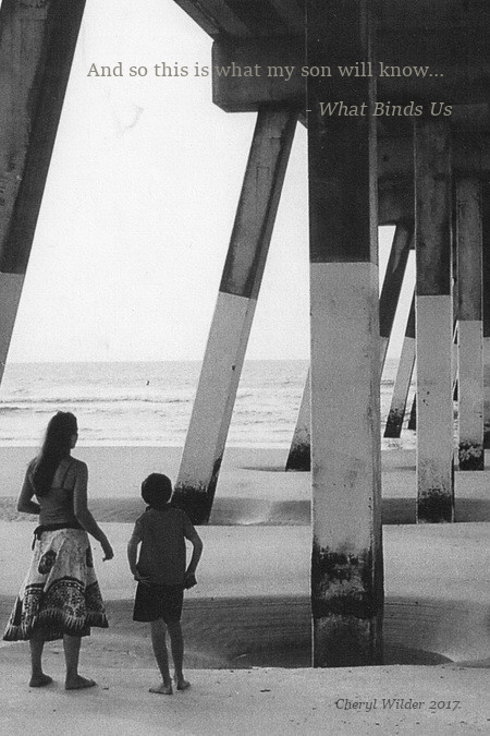 mother and young son stand underneath ocean pier