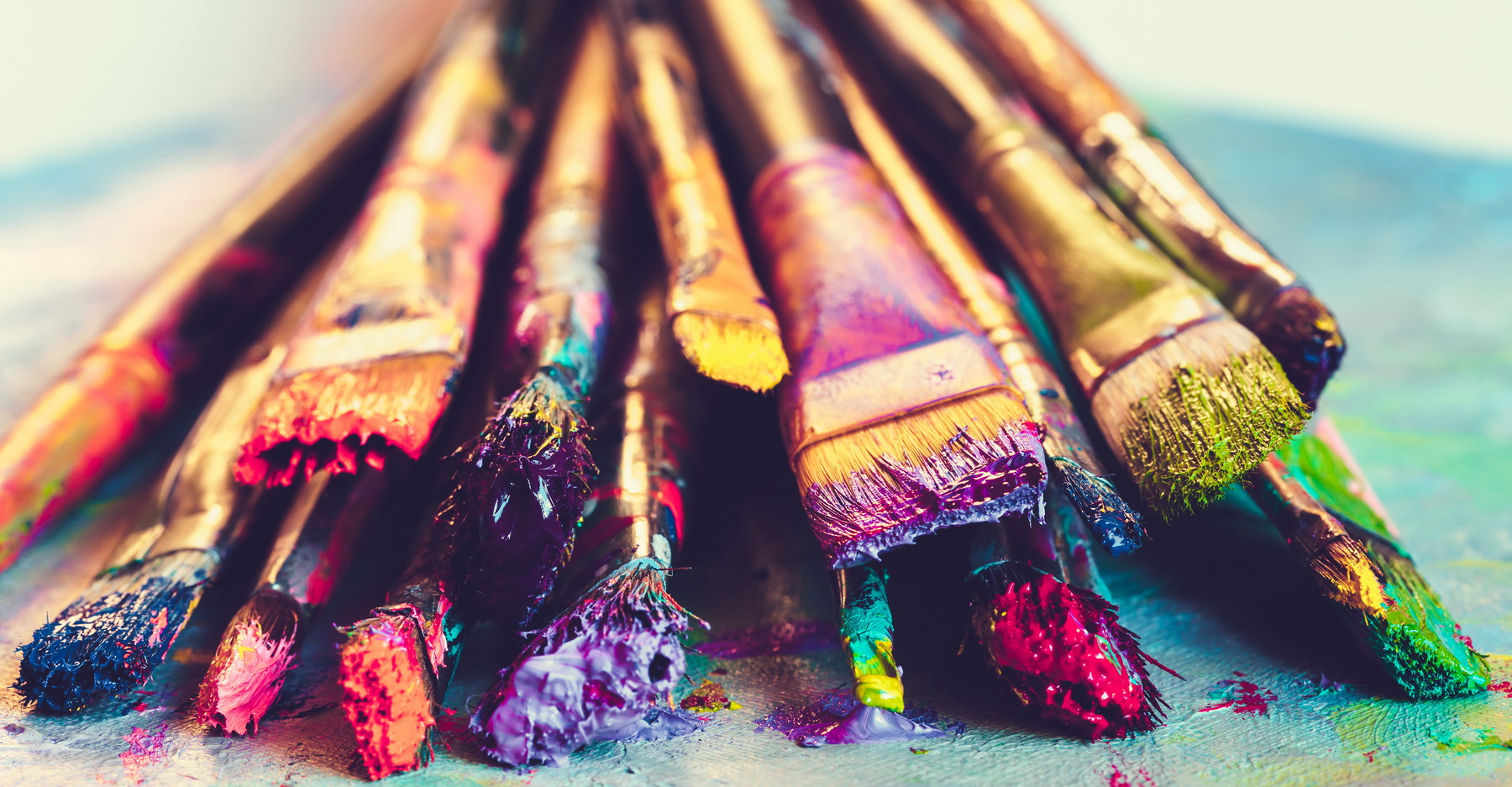 paintbrushes full of vibrant paint colors lined up in a pile on a table