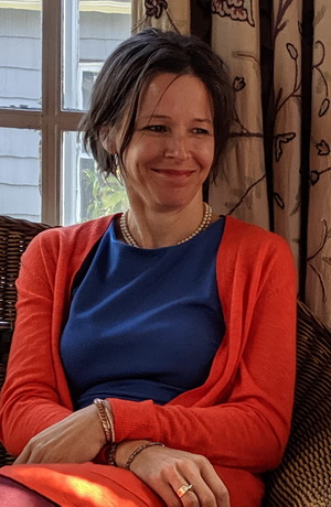 woman in sitting room wearing blue dress and burnt orange sweater